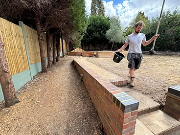 Curved red brick retaining wall with stone coping alongside a sandy construction path in Surrey