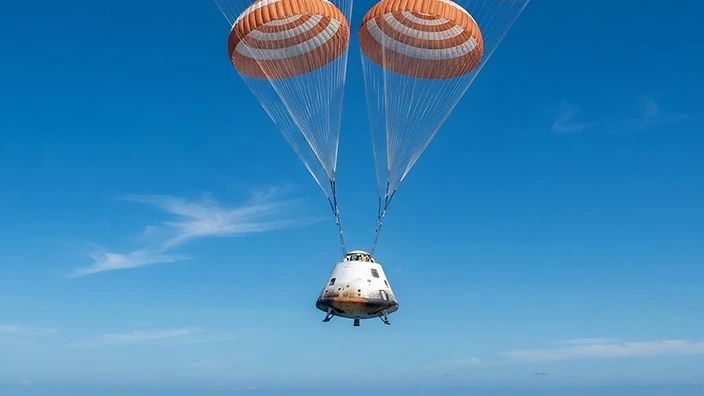 A crewed spacecraft capsule descending under parachutes