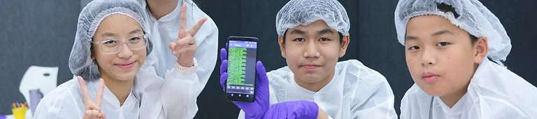 Four students in lab coats debugging code on a device