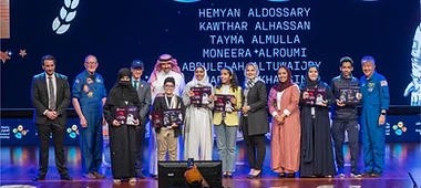 Graduates and NASA astronauts posing on stage with framed certificates at an awards ceremony