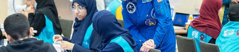NASA mentor guiding students through a hands-on laptop workshop