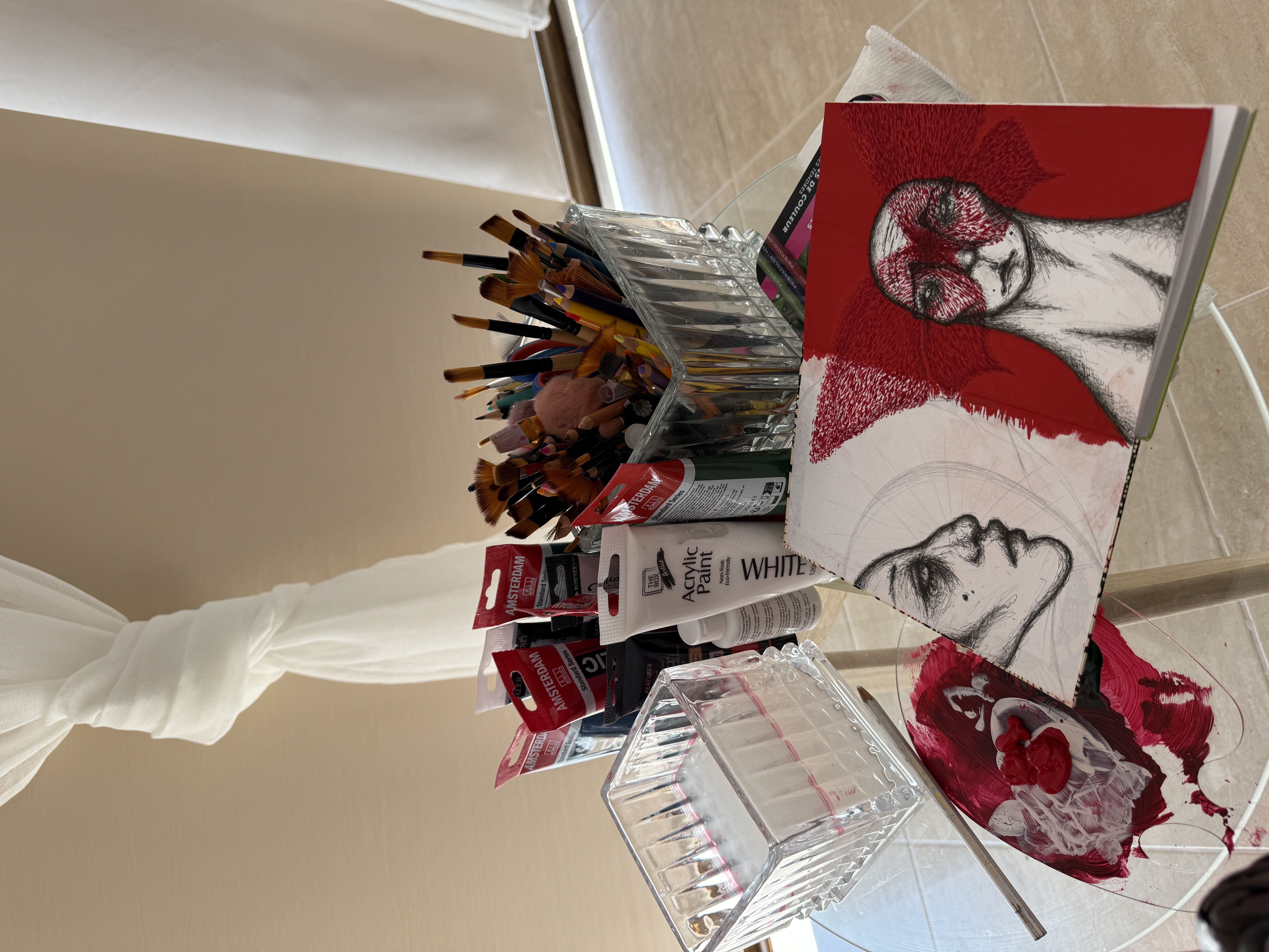 Studio table with paints, brushes and a red and white sketchbook