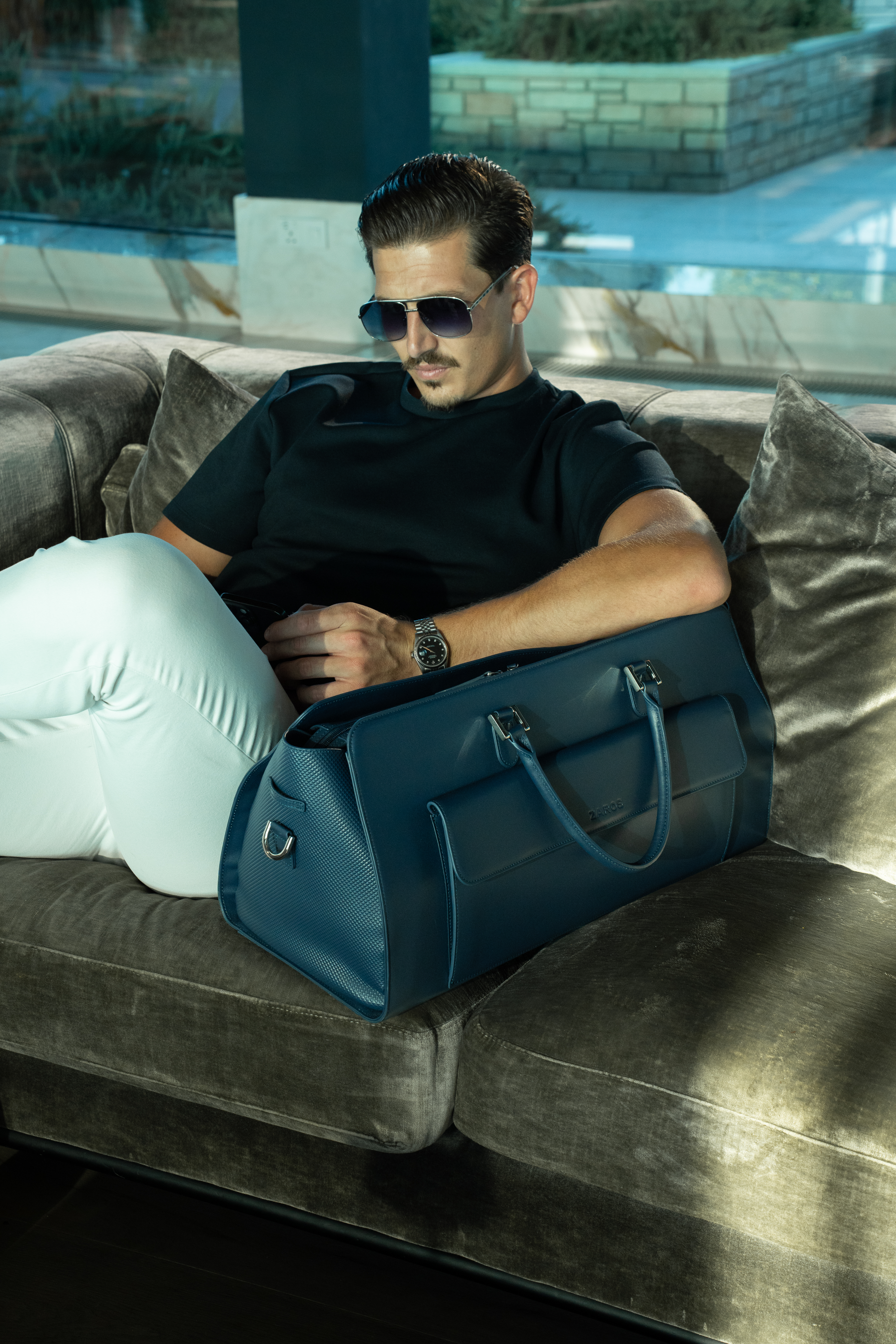 Man seated on a velvet sofa with a ZAROS holdall