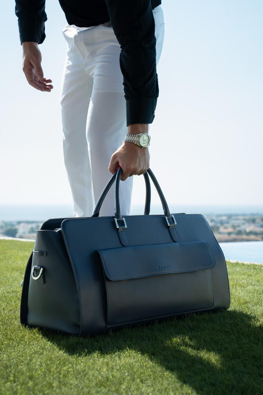 Man holding a ZAROS leather holdall on a lawn above the sea