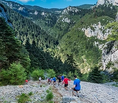 Trail runners navigating a rocky slope on Mount Parnassos above a forested valley