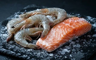 Fresh frozen salmon and prawns on dark wet slate with ice crystals