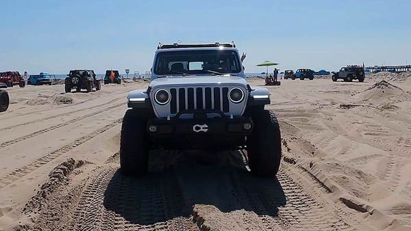 A white Jeep Wrangler driving on the beach at Ocean City Jeep Fest with tire tracks in the sand