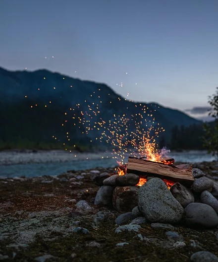 A campfire flickering on a rocky riverbank at dusk - light for the path ahead.