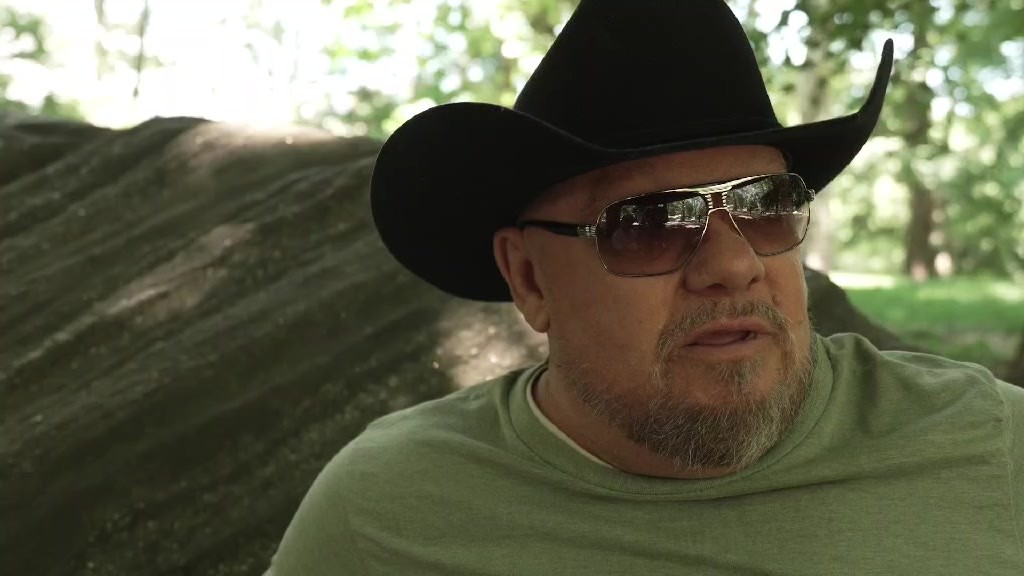 Glenn Baker in a black cowboy hat and green shirt speaking outdoors