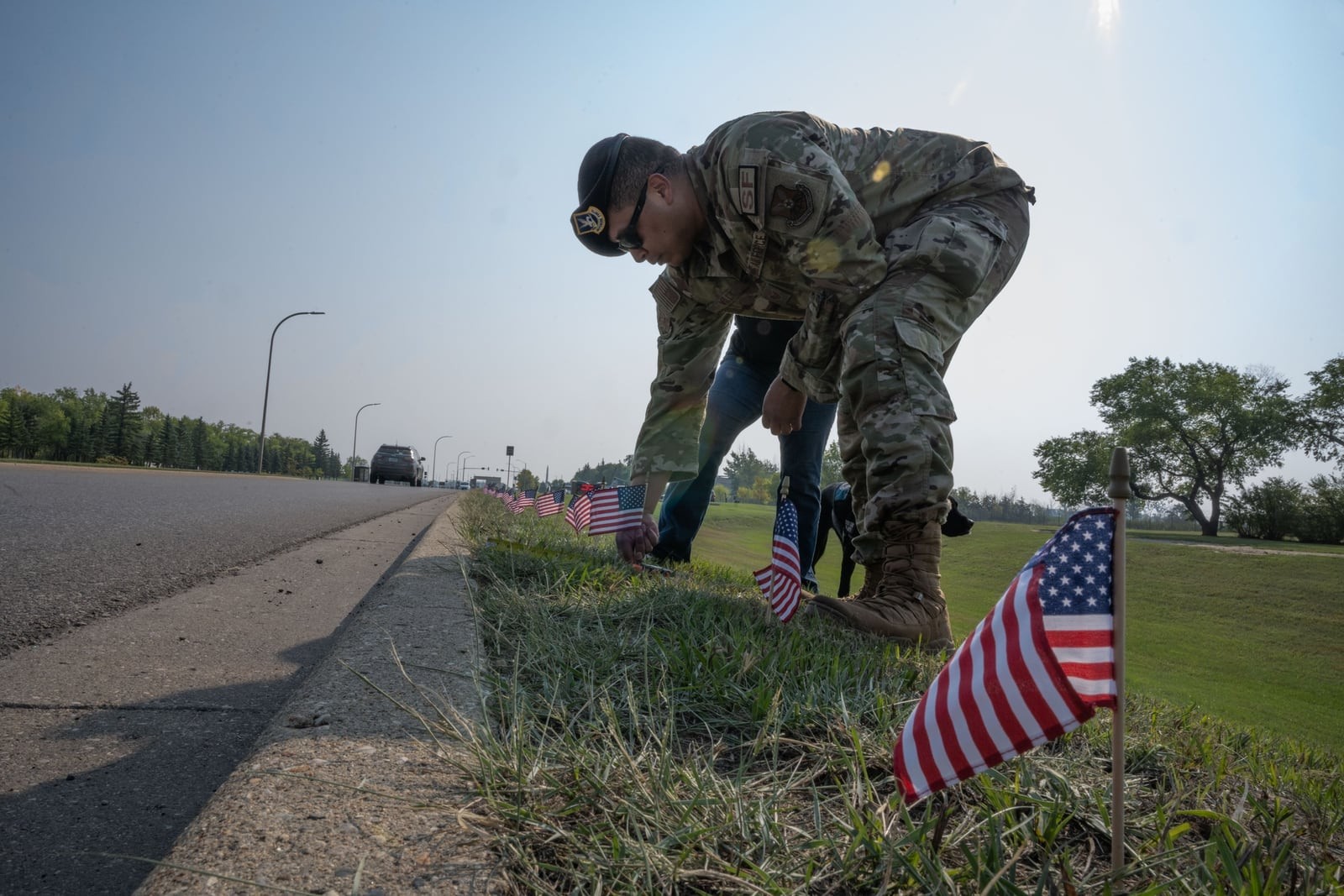 An airman in uniform plants a small American flag along a road at Minot Air Force Base