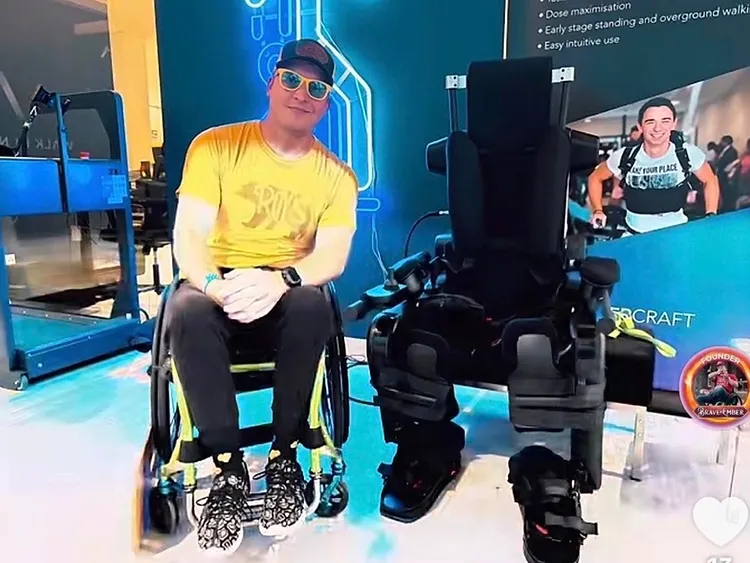 Joshua Holm seated in his wheelchair beside a Wandercraft exoskeleton — the technology this campaign funds