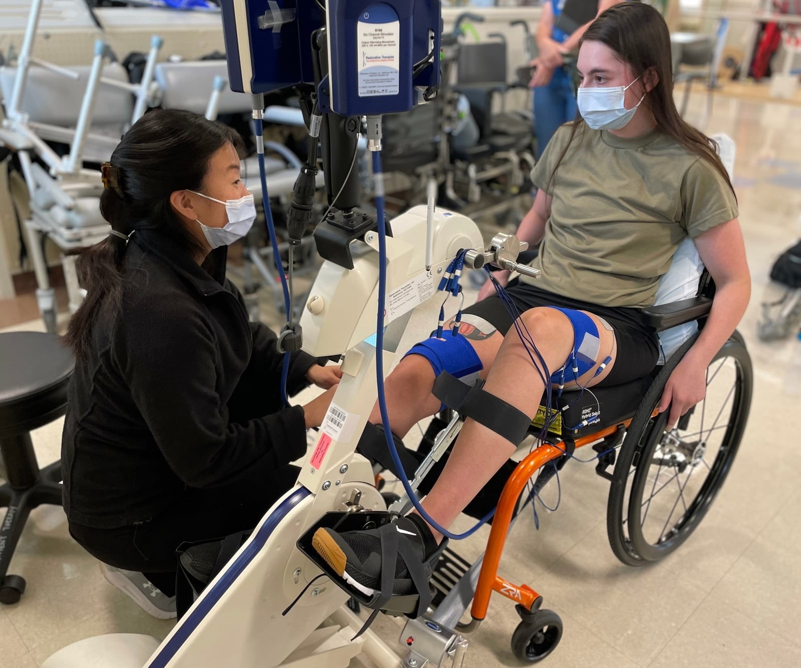 A physical therapist connects an airman in a wheelchair to a stationary rehabilitation cycle