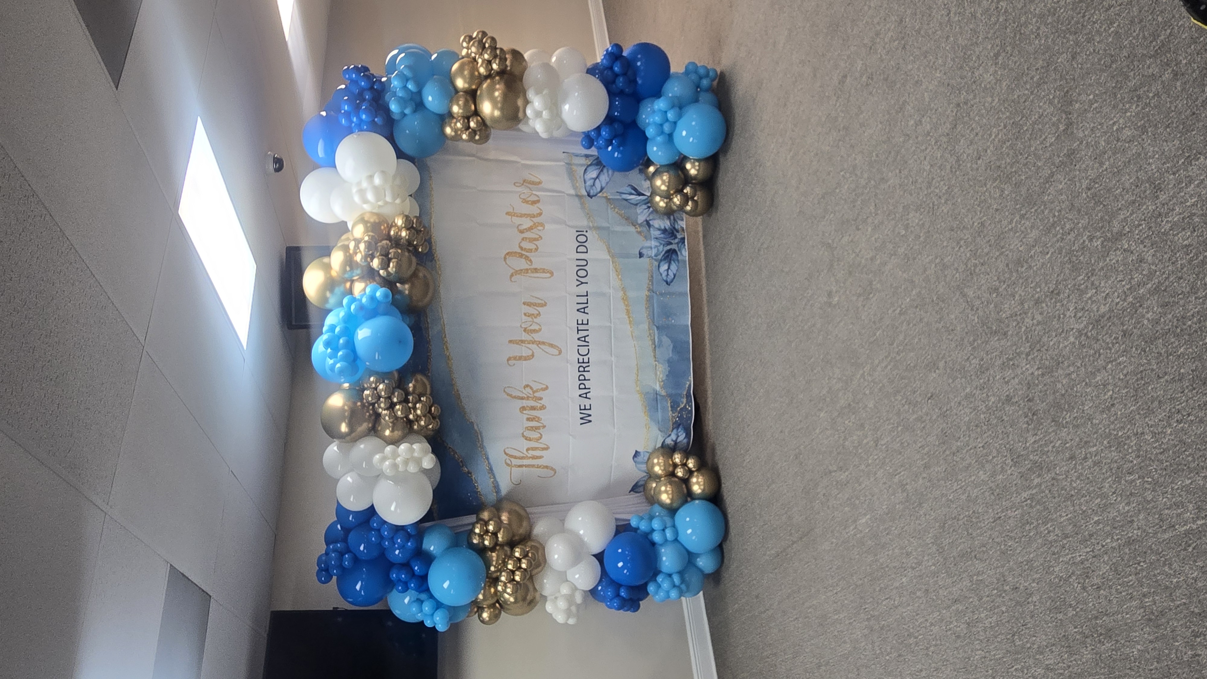 Thank You Pastor balloon arch in royal blue, white and metallic gold framing a scripted appreciation banner