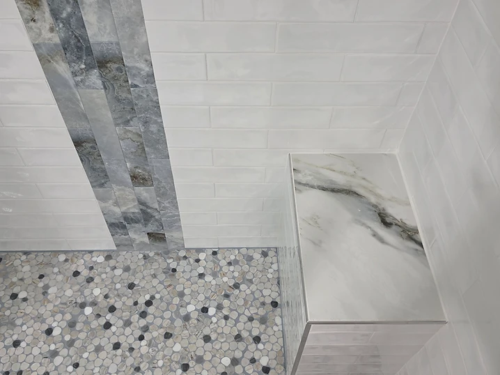 Finished shower corner showing a marble niche, stone accent band, and pebble mosaic