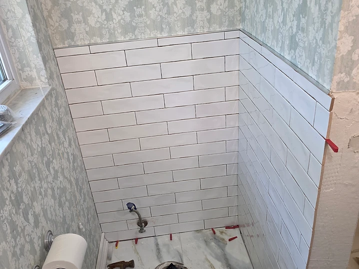 White subway tile installed on a shower wall with red leveling spacers