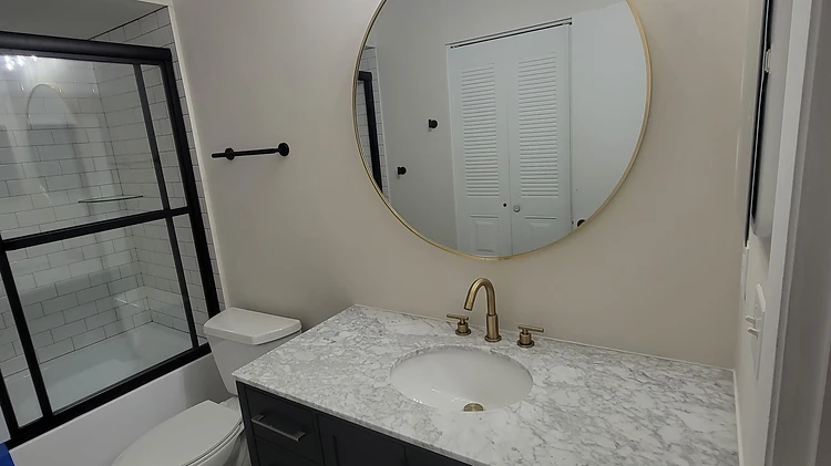 Completed bathroom remodel with a black vanity, round mirror, gold fixtures and patterned black-and-white floor in Largo, FL
