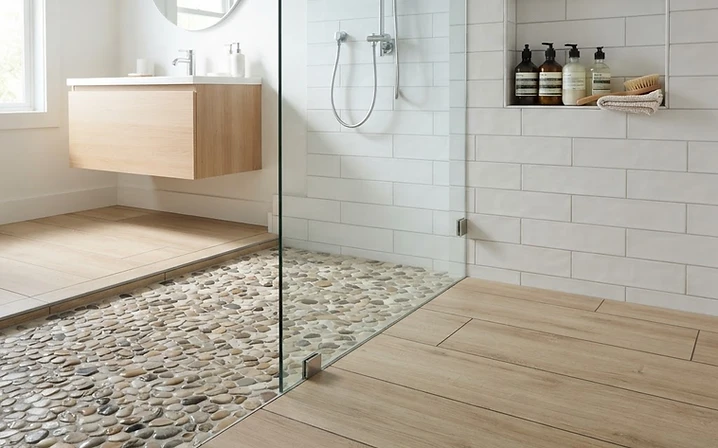 Bathroom tile flooring meeting a pebble-style shower floor with a built-in storage niche