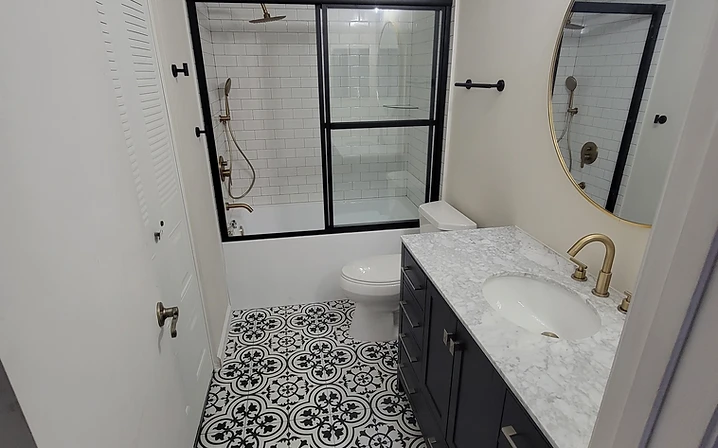 Completed bathroom remodel with a black vanity, round mirror, gold fixtures, patterned flooring and black-framed shower in Largo, FL