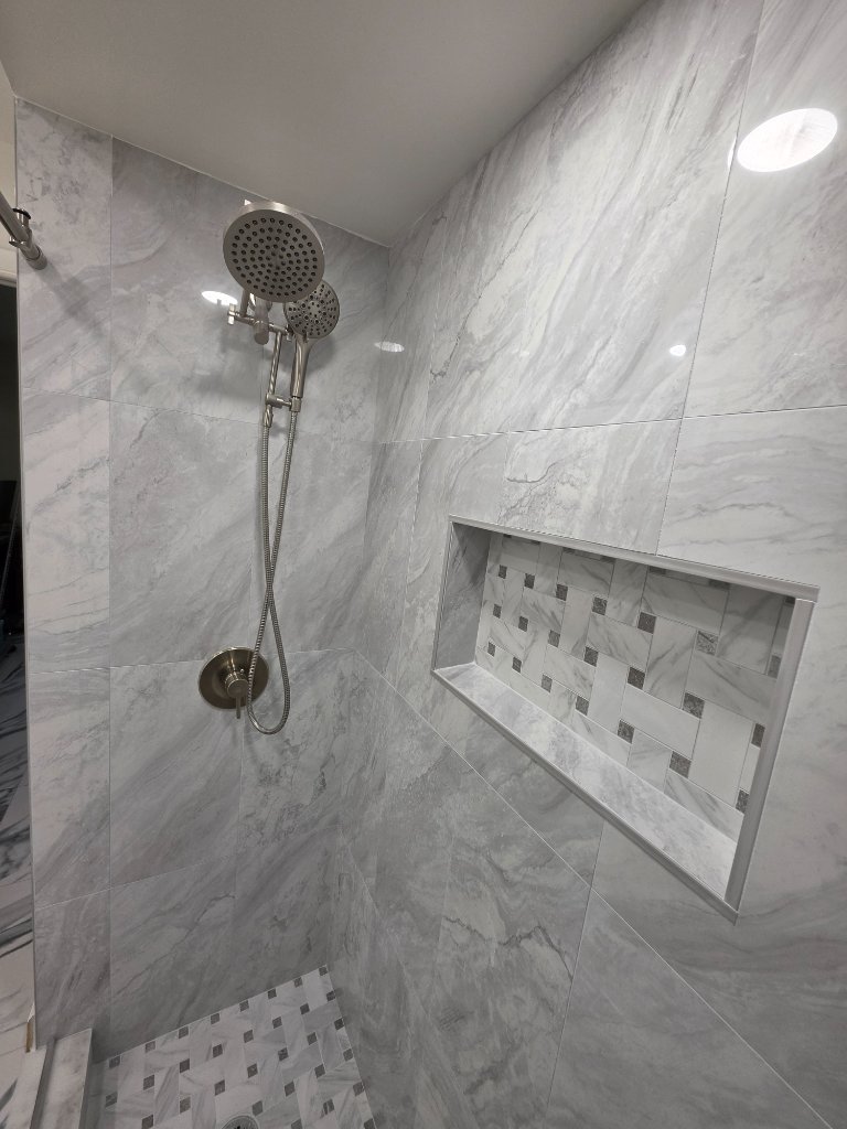 Final finished shower showing brushed nickel dual showerhead, custom mosaic niche, and mosaic floor