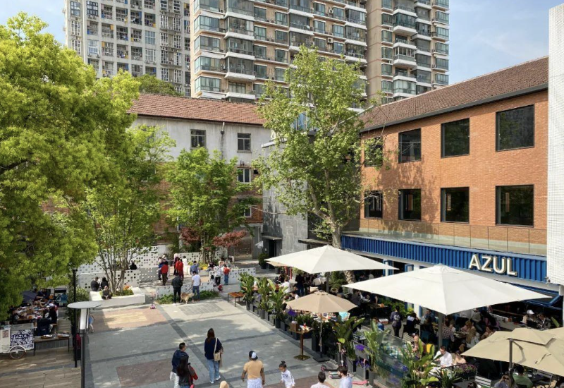 Shankang Li from above — the blue AZUL terrace, white umbrellas, and the apartment towers rising behind.