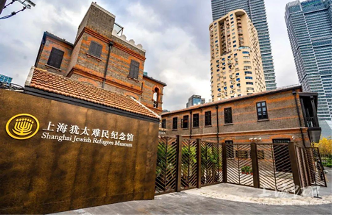 The Shanghai Jewish Refugees Museum — a bronze wall inscribed with a gold menorah and the museum's name, beside a red-brick historic building