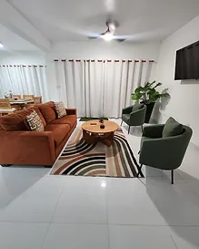 Bright open-plan living room with terracotta sofa, green armchairs, and white tile floors in a turn-key Costambar condo