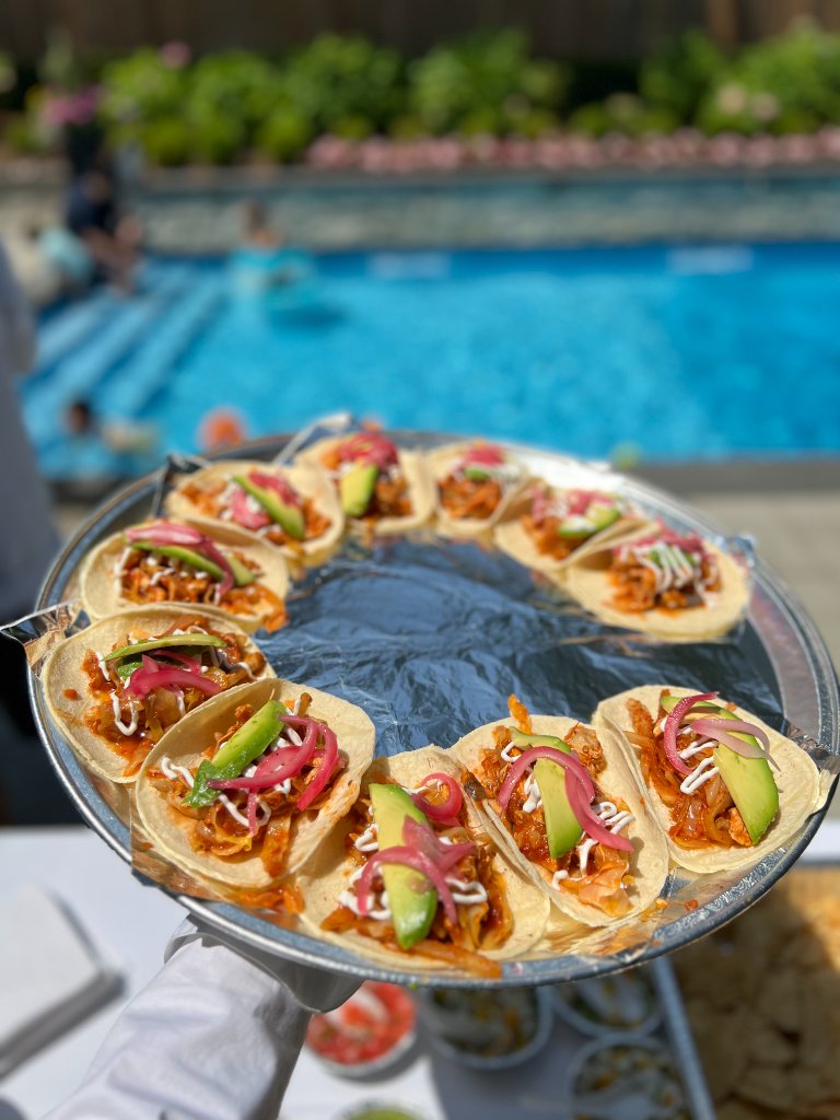 Tacos arranged on silver tray held beside a swimming pool