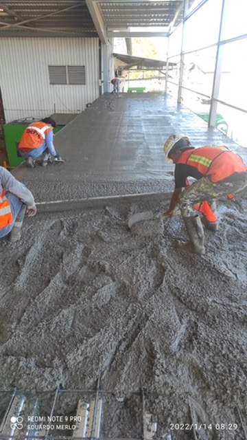 Trabajadores con chaleco de seguridad nivelando concreto sobre plataforma de acero reforzado