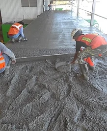 Trabajadores con chaleco de seguridad nivelando concreto sobre plataforma de acero reforzado