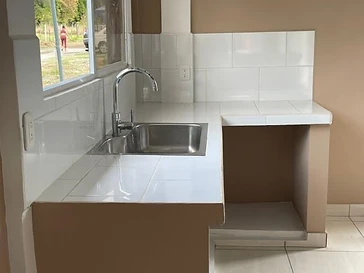 Cocina residencial terminada con mostrador de azulejo blanco, fregadero de acero inoxidable y grifería cromada.