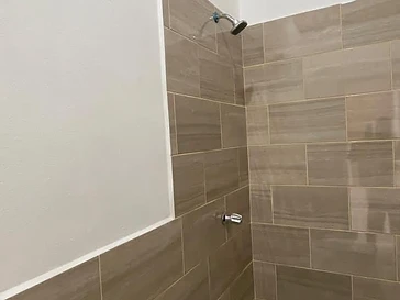 Baño residencial terminado con pared de cerámica tono madera, regadera cromada y piso cerámico claro.