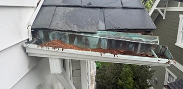Corroded, debris-packed gutter separating from the roof edge — a failing system that needs repair or replacement