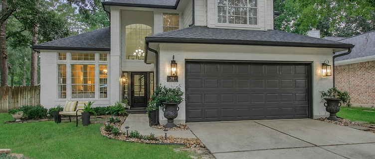 Two-story home in The Woodlands surrounded by tall pines with new seamless gutters protecting the roofline