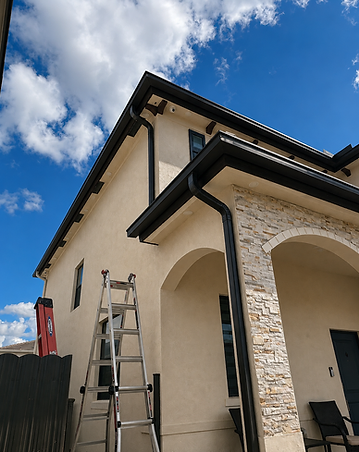Black seamless gutters custom-formed on a two-story stucco home, with clean corners and a downspout on every roofline