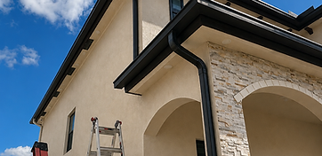 Black seamless gutters custom-formed on a two-story stucco home, with clean corners and a downspout on every roofline