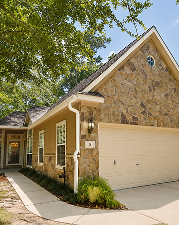 Complete gutter system — seamless gutters and color-matched downspouts — installed on a stone Woodlands home under mature trees