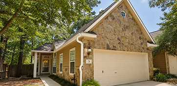 Complete gutter system — seamless gutters and color-matched downspouts — installed on a stone Woodlands home under mature trees