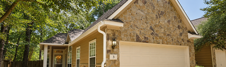 Complete gutter system — seamless gutters and color-matched downspouts — installed on a stone Woodlands home under mature trees