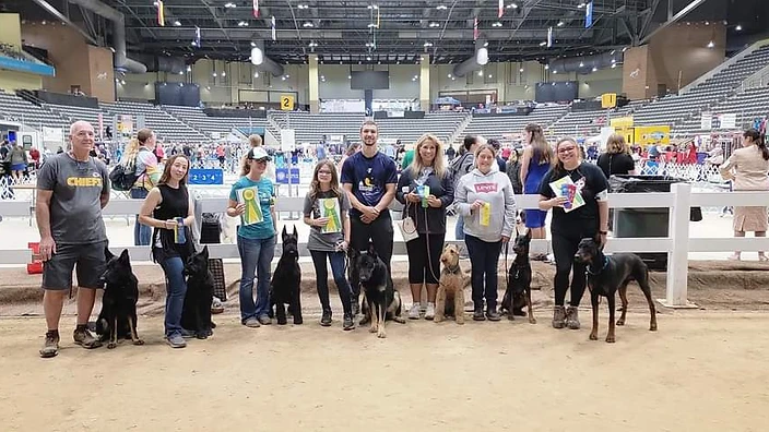 Start Now Dog Training clients with their dogs at a competition, showing off their ribbons and achievements.