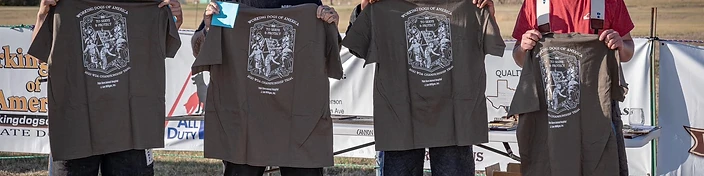 Four trainers holding up Working Dogs of America championship t-shirts at a trial.
