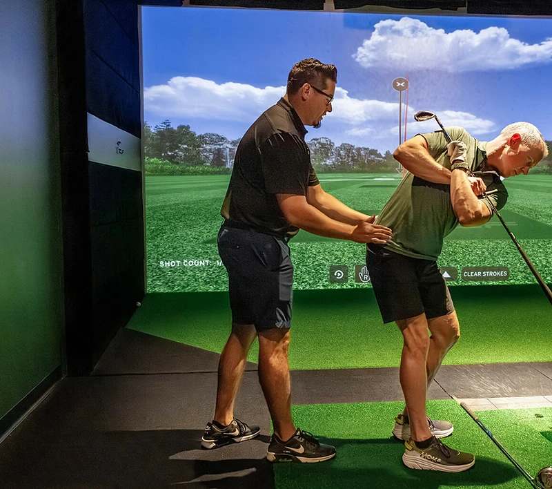 Coach Jason Cole giving a hands-on lesson in the X-Golf simulator bay