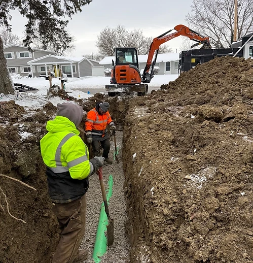 Two Alfieri Brothers crew members working in a trench with an excavator in the snow