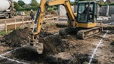 Excavator digging the foundation trench with traced lines on the soil