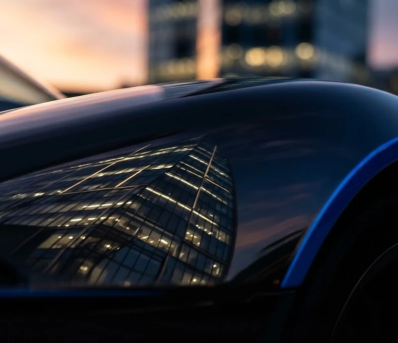 Glossy black sports car fender reflecting a sunset