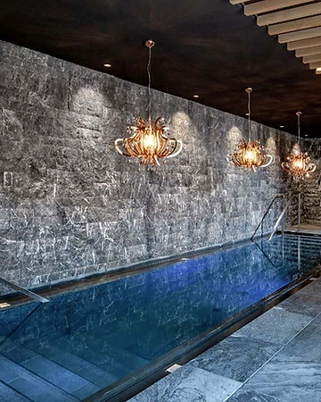 Indoor swimming pool at Gardena Grödnerhof Hotel & Spa with branch-like chandeliers and a stone feature wall