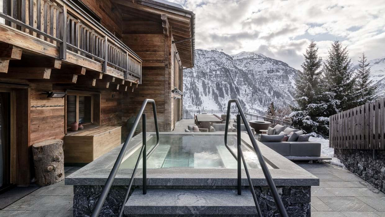 The Arula Chalets outdoor spa terrace with a stone hot tub and panoramic mountain views over Lech