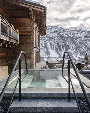 The Arula Chalets outdoor spa terrace with a stone hot tub and panoramic mountain views over Lech