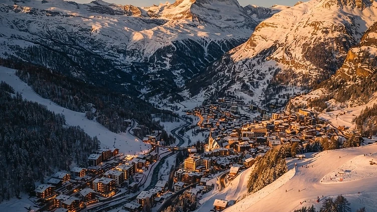 Aerial golden-hour panorama of a ski resort village nestled among alpine peaks