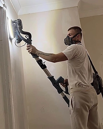 Kieran P Blanchard sanding a wall with a pole sander