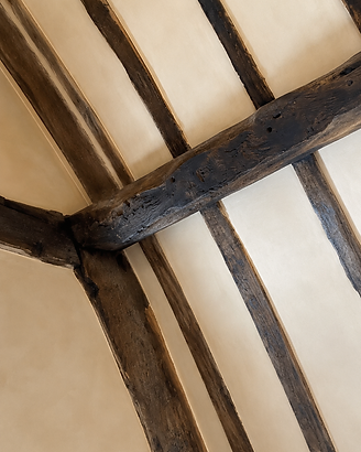 Lime-washed plaster infill panels where the timber framing meets the ceiling, the colour deepening across the surface
